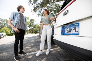 two students stand at the trunk of a car with the Argos license plate
