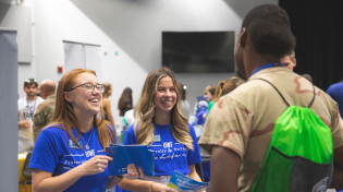 two female students are tabling at 2022 Orientation and speaking with a male student
