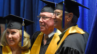 Three alumni stand together in black cap and gown with a gold sash designating them as 50 year graduates.