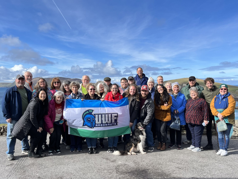 A group of alumni and guests pose in Ireland on the bluffs with a UWF Flag