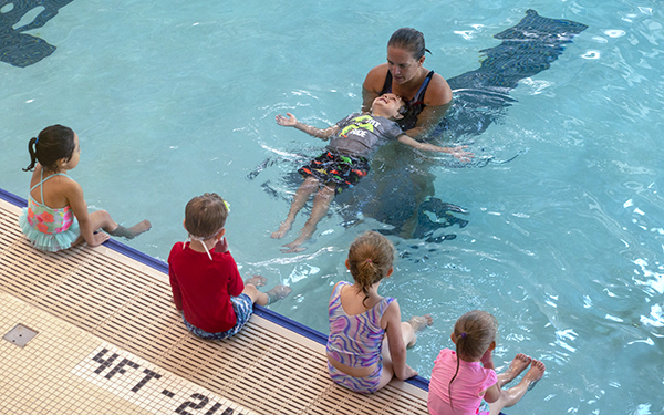 A child is learning to float on his back with help from the swim instructor during a swim lesson.
