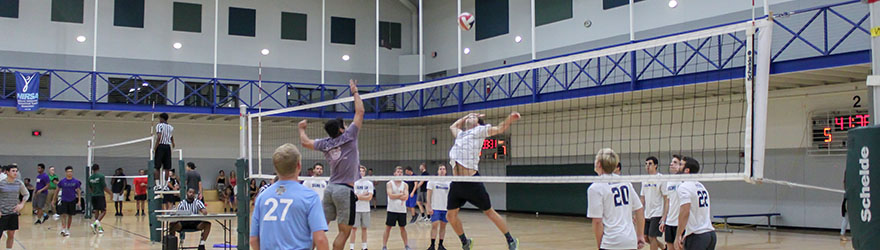 Students participating in Intramural Sports Volleyball tournament: two students on either side of the net are jumping for the volleyball.