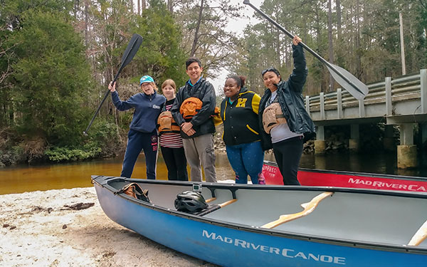 Participants on the canoe trip posing together, holding up canoe oars and smiling at the camera. 