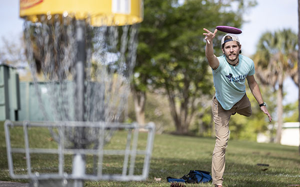 Student throwing a disc towards the basket on the UWF disc gold course
