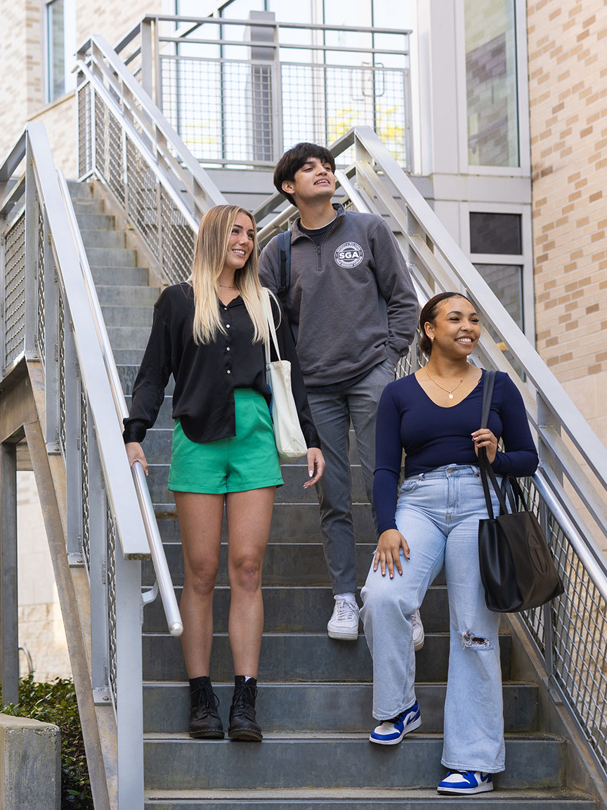 Three UWF students descend outdoor stairs on campus.
