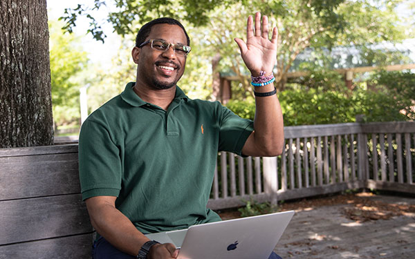 Admissions counselor Nate Benton, Jr. sits at a bench on campus and waves.