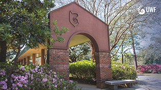 Brick archway surrounded by trees and flowering bushes.
