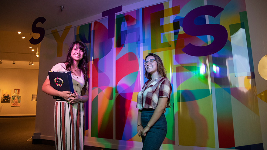 Students in front of the Synthesis exhibition title wall