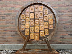 A wooden ring art piece with panels of different faces displayed inside the ring.