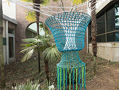 A rope art piece displayed outdoors between building walls in front of a few trees.