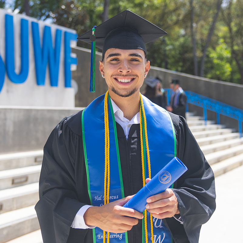 Smiling student wearing graduation cap & gown at the UWF entrance plaza