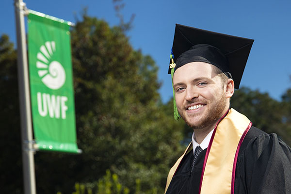 A UWF graduate smiles while wearing cap and gown.