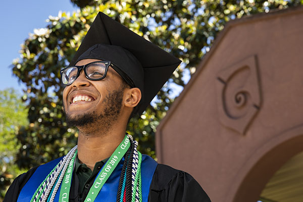 A UWF graduate smiles while wearing cap and gown.
