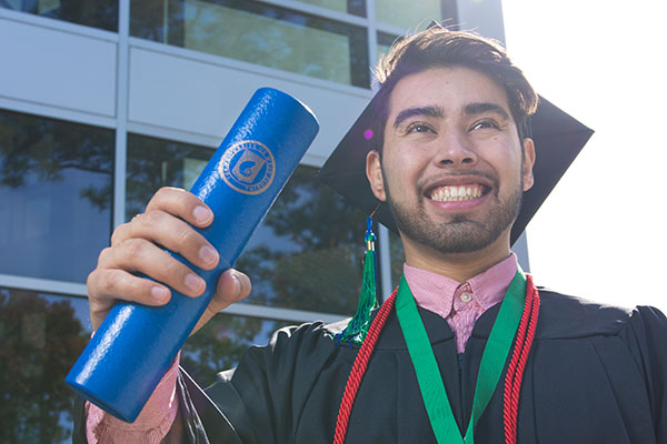 A UWF graduate smiles while wearing cap and gown and holding a diploma case.