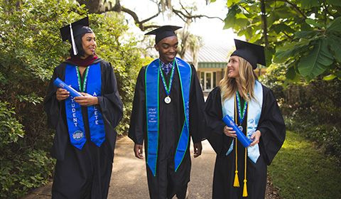 Three students in cap and gown participate in a graduation photo shoot.