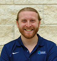 Jonathan Lee outdoor headshot wearing a blue polo against a tan brick wall.