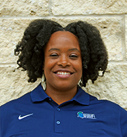 Nadya Collins outdoor headshot wearing a blue polo against a tan brick wall.