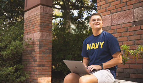 A UWF veteran student uses a laptop by the Canto al Sol archway.