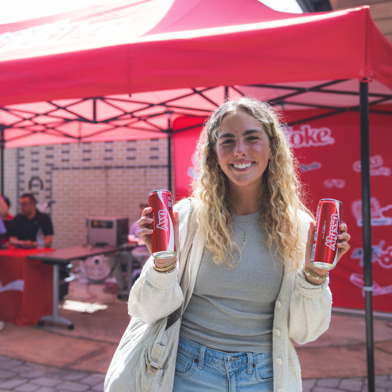 student holding 2 cans of coke with names on them