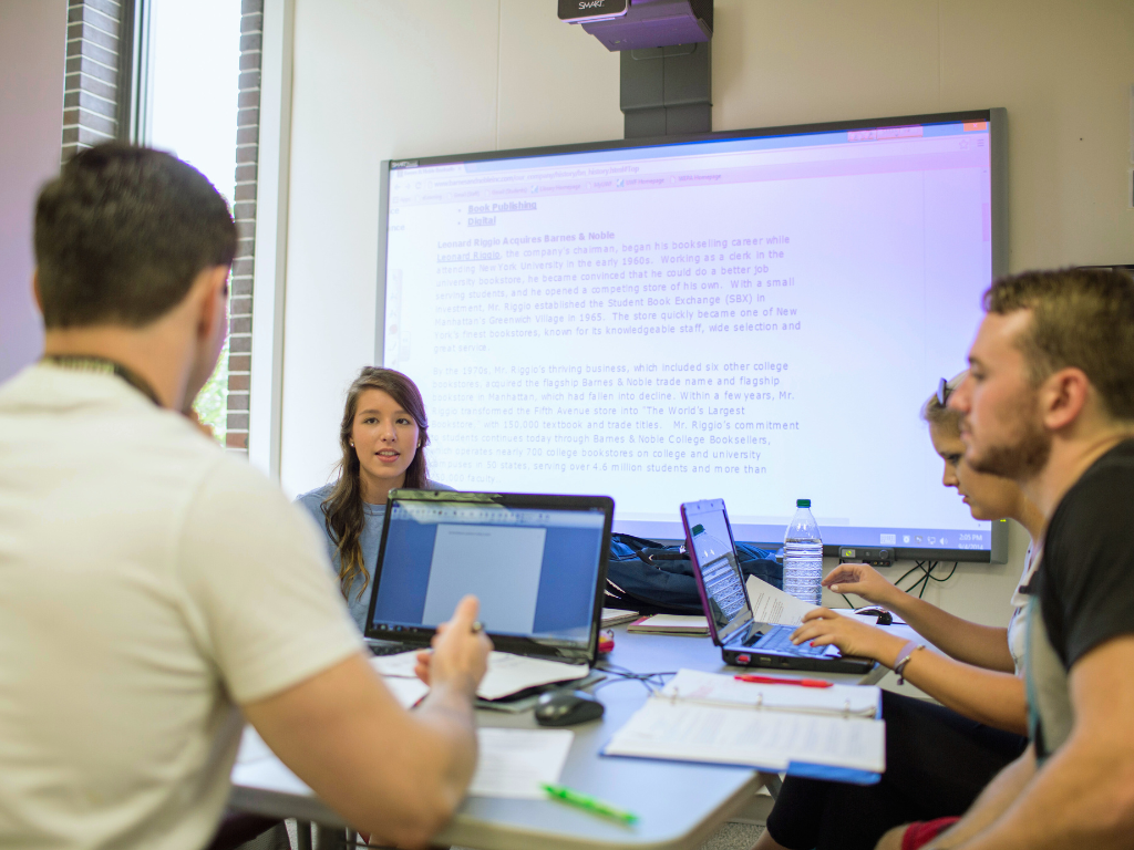 Students are gathered around an interactive whiteboard studying