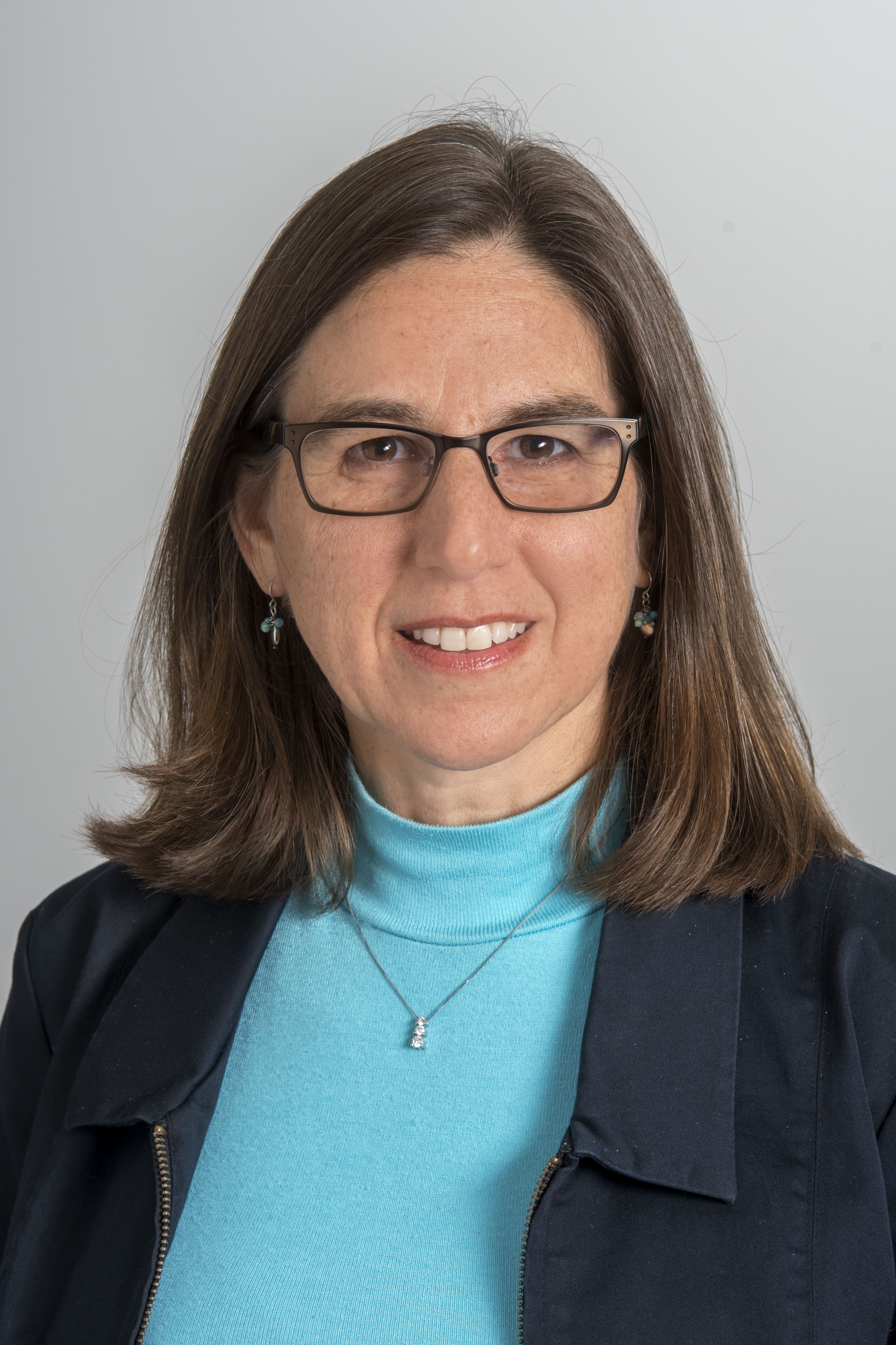 Elizabeth Arthur indoor headshot in a bright blue top under dark blue top against a light gray background.