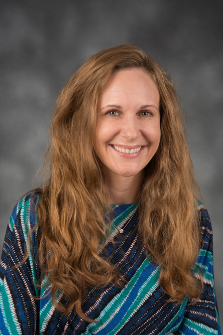 Leasha Barry indoor headshot in a blue, green, and gold striped top against a gray background.