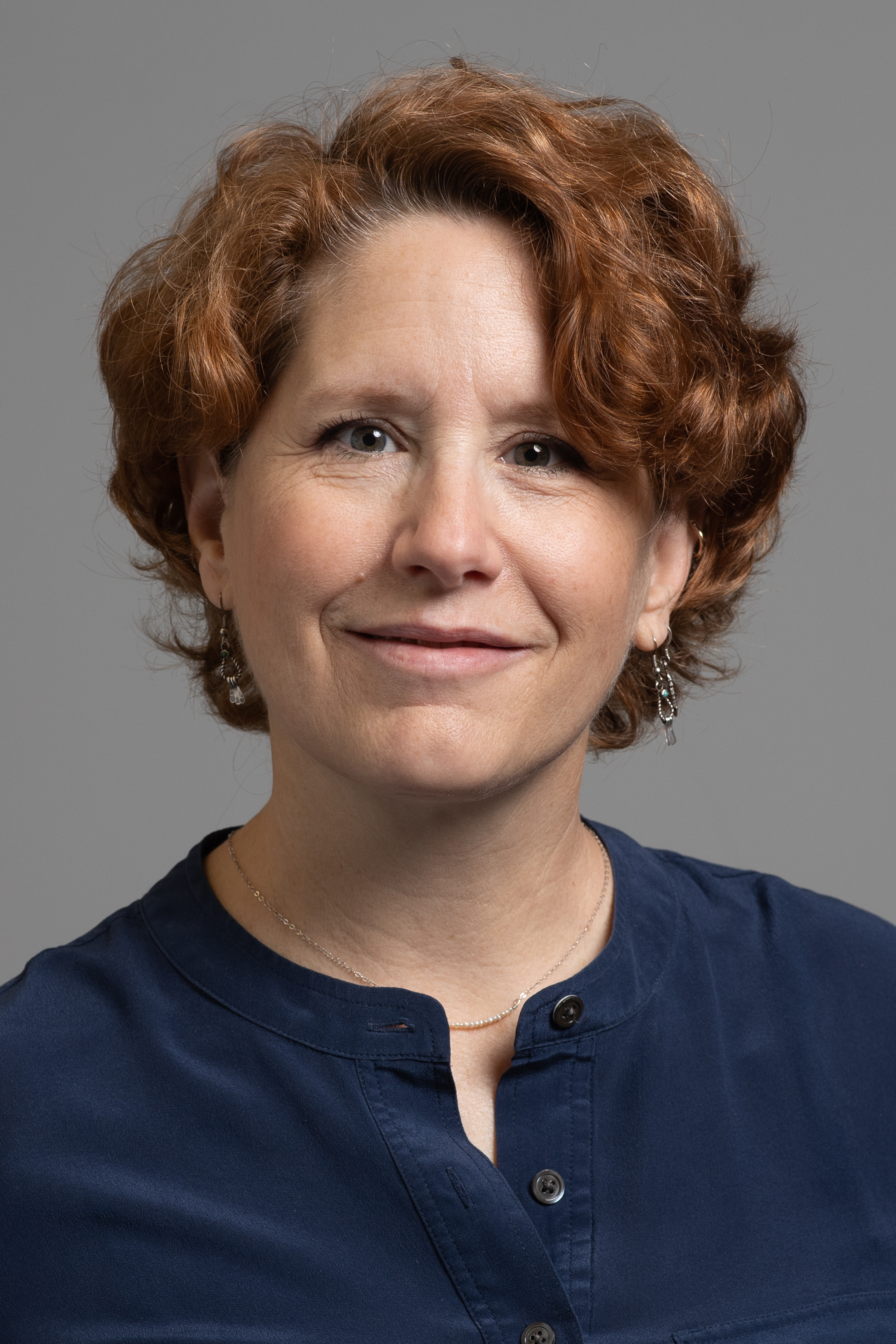 Mary Ann Scott indoor headshot dark blue button top against a gray background.
