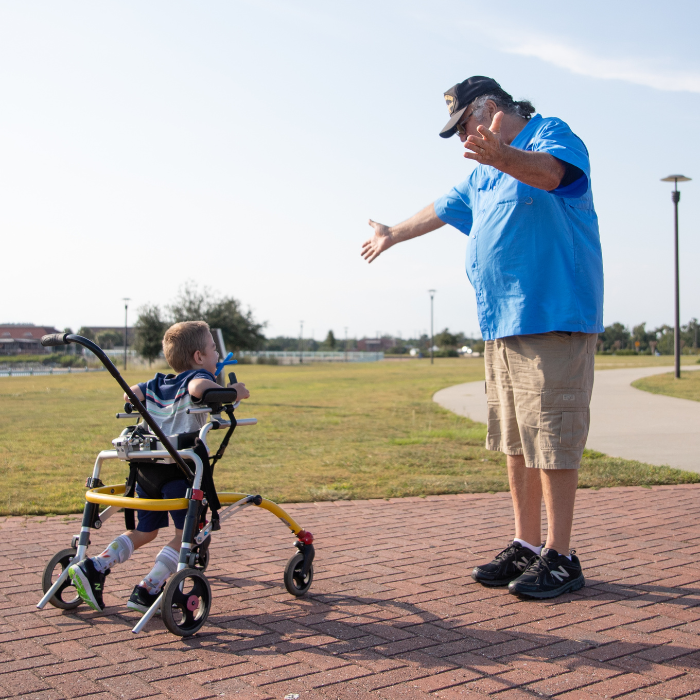 A young child using a walker while a volunteer cheers them on