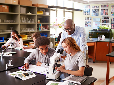 Science teacher in the classroom with students looking at microscope