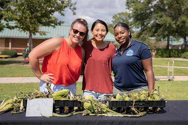 Students and staff member standing in front of a corn booth for Argo Pantry food market event