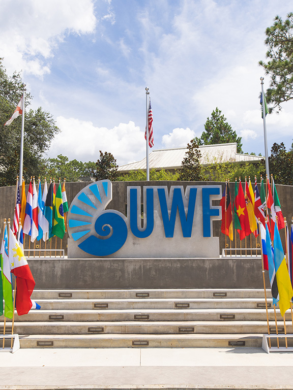 UWF campus entrance monument sign with stands of international flags displayed around it.