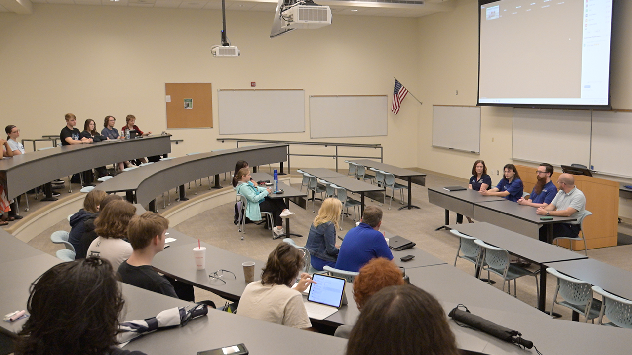 People sitting in stadium seating lecture hall listening to a speaker