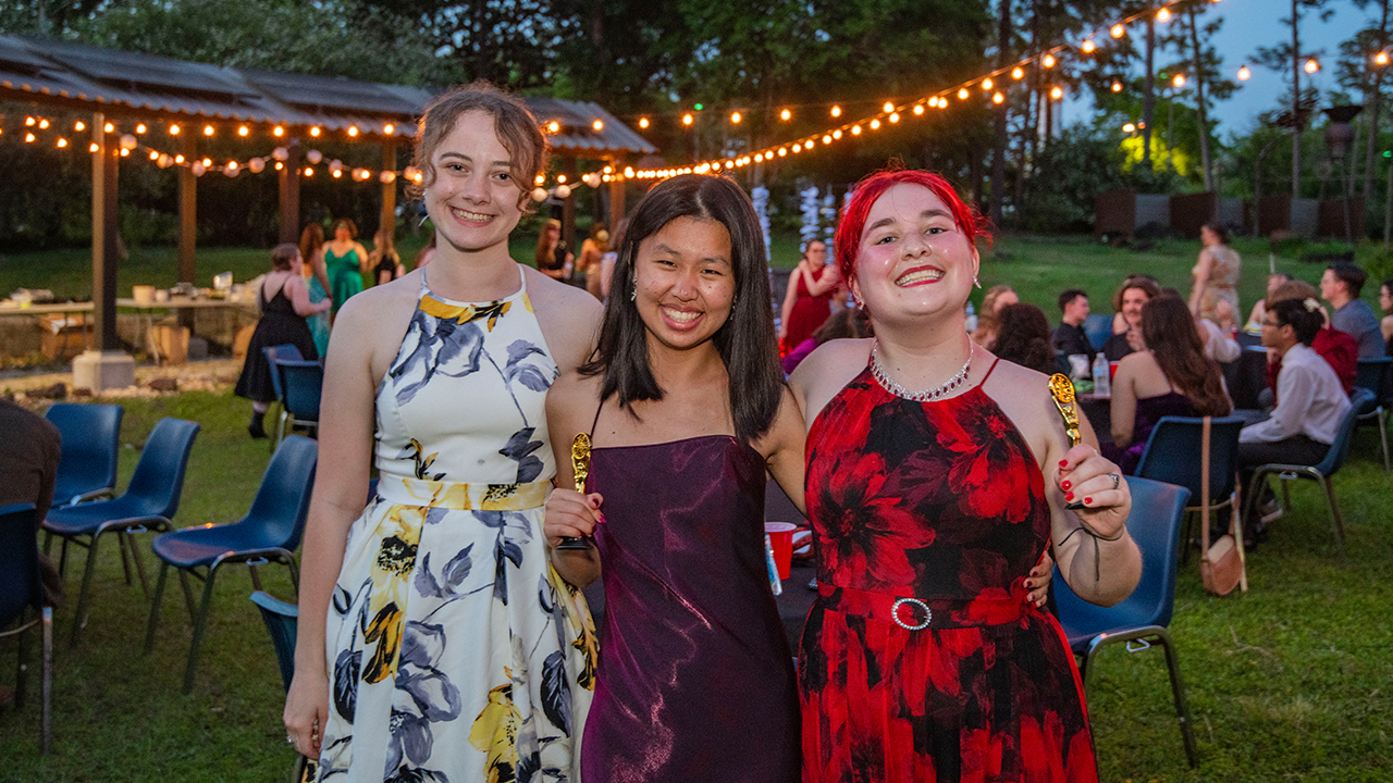 Three people standing together for a photo at an outdoor event at dusk