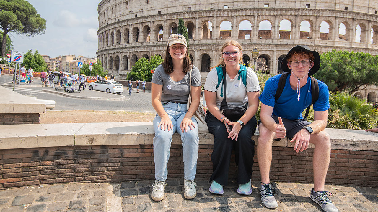 People sitting on a wall in front of the Colosseum in Rome, Italy