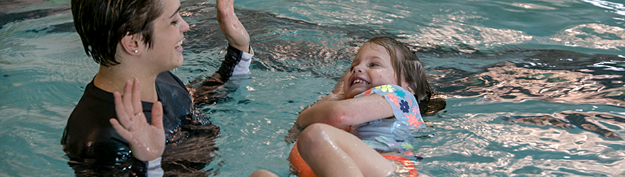 A swim instructor is holding her hands up as if she just let go of her student who is happily learning how to float