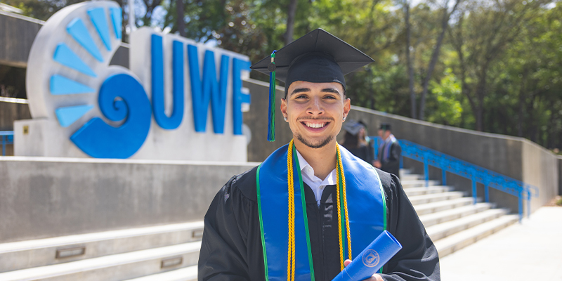 student posing in their graduation regalia at front entrance