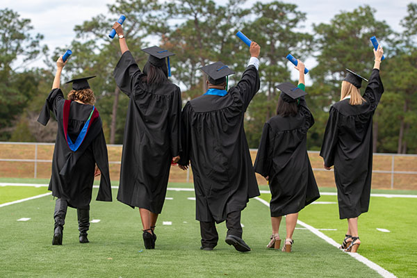 Five students in graduation regalia on PenAir Field on the UWF Pensacola campus.