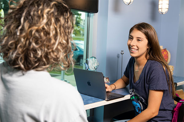 Student using a laptop while conversing with another student.