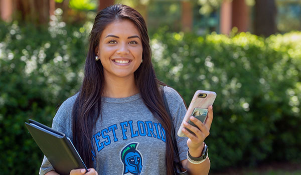 A UWF student smiles while holding books and a phone.
