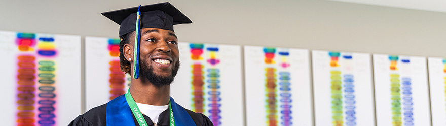 A UWF graduate smiles while wearing cap and gown in the Lab Sciences Annex.