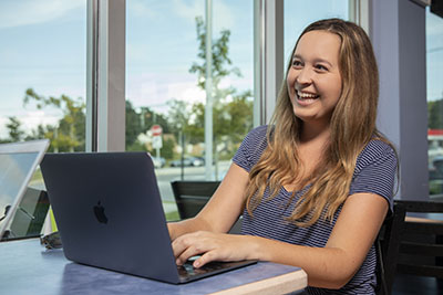 A UWF student smiles while using a laptop indoors.