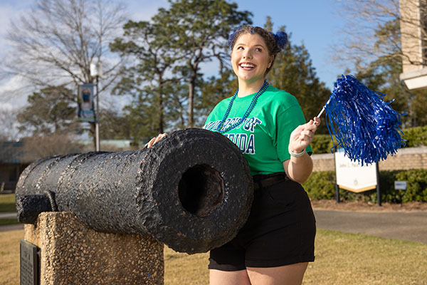A UWF student smiles while waving a pom-pom and touching the cannon on the Cannon Green.