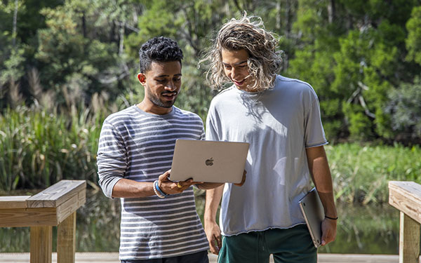 Two students use a laptop while standing on the dock at Thompson Bayou.