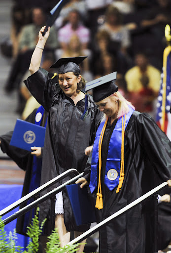 A student in graduation cap and gown attire raises an arm in celebration after walking across the commencement stage.