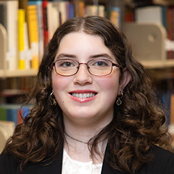 Elizabeth Ellis indoor headshot in business attire against a shelf of books in a library.