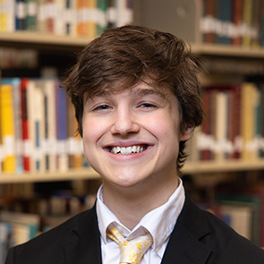 James Treick indoor headshot in suit and tie attire against a shelf of books in a library.