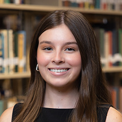 Kamryn Gibbs indoor headshot in business attire against a shelf of books in a library.