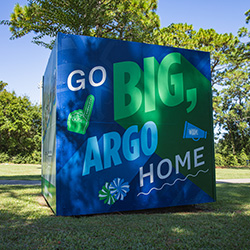 Outdoor cube mural with one side displaying a UWF themed Go Big, Argo Home artwork.