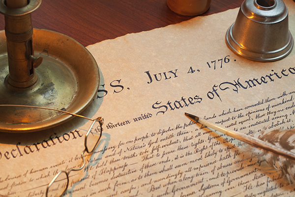 A quill pen, vintage-style spectacles and a vintage-style candlestick on the Declaration of Independence.