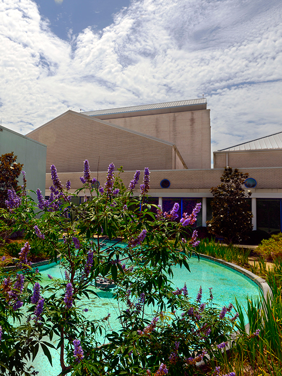 The UWF Center for Fine and Performing Arts building with a fountain and blooming flowers in the front of the building.
